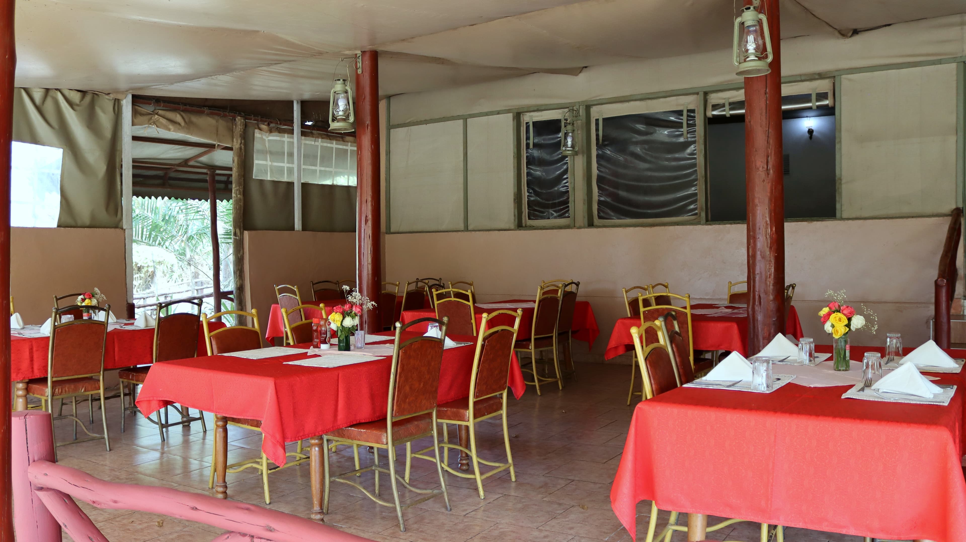 A dining room laid with red tablecloths, flowers and folded napkins at Lake Naivasha Crescent Camp