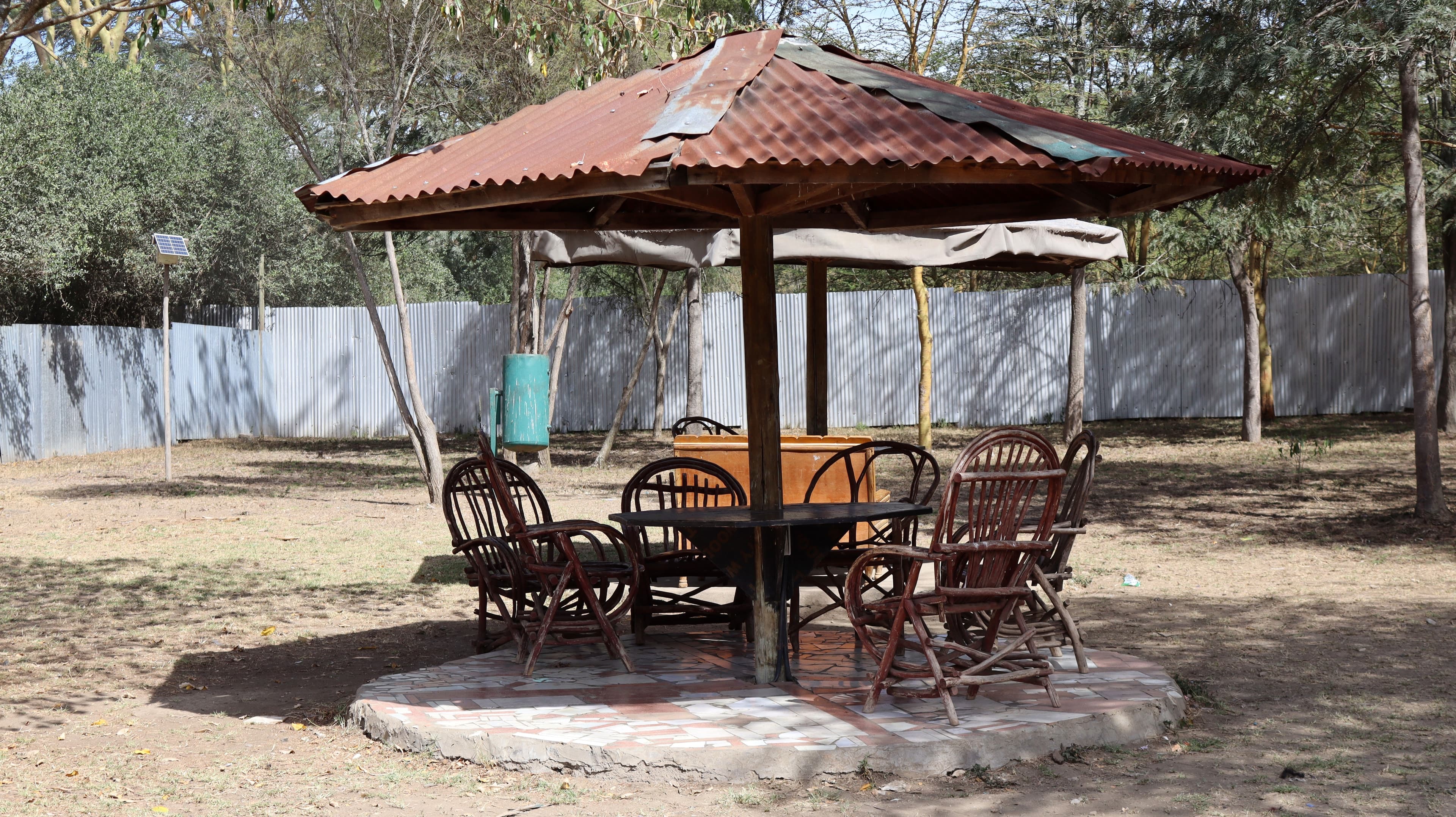 Wooden chairs around a table under a shaded roof in the grounds of Lake Naivasha Crescent Camp