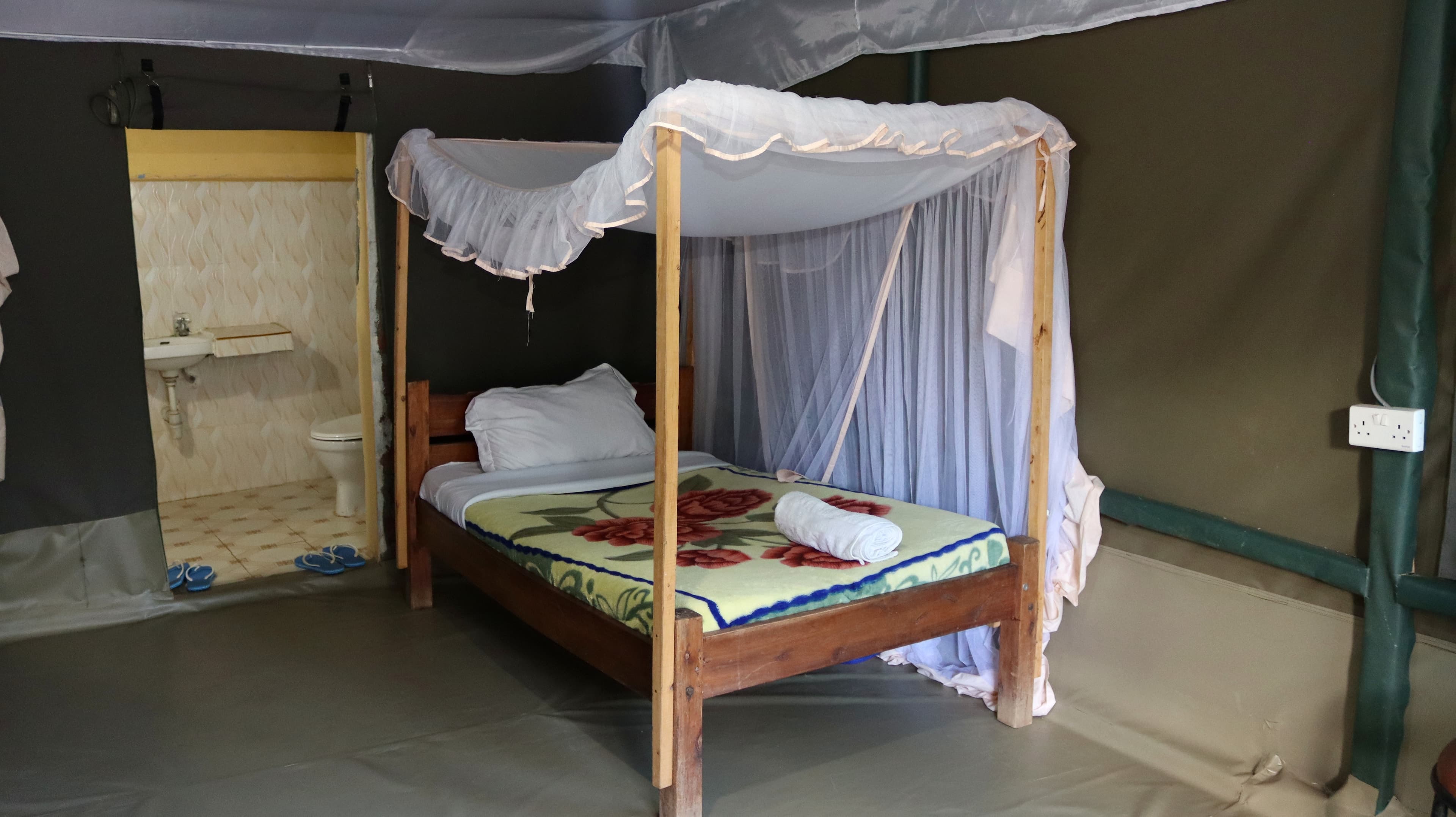 A bed under a mosquito net, with a tiled bathroom visible through a doorway, inside a guest tent at Miti Mingi Eco Camp