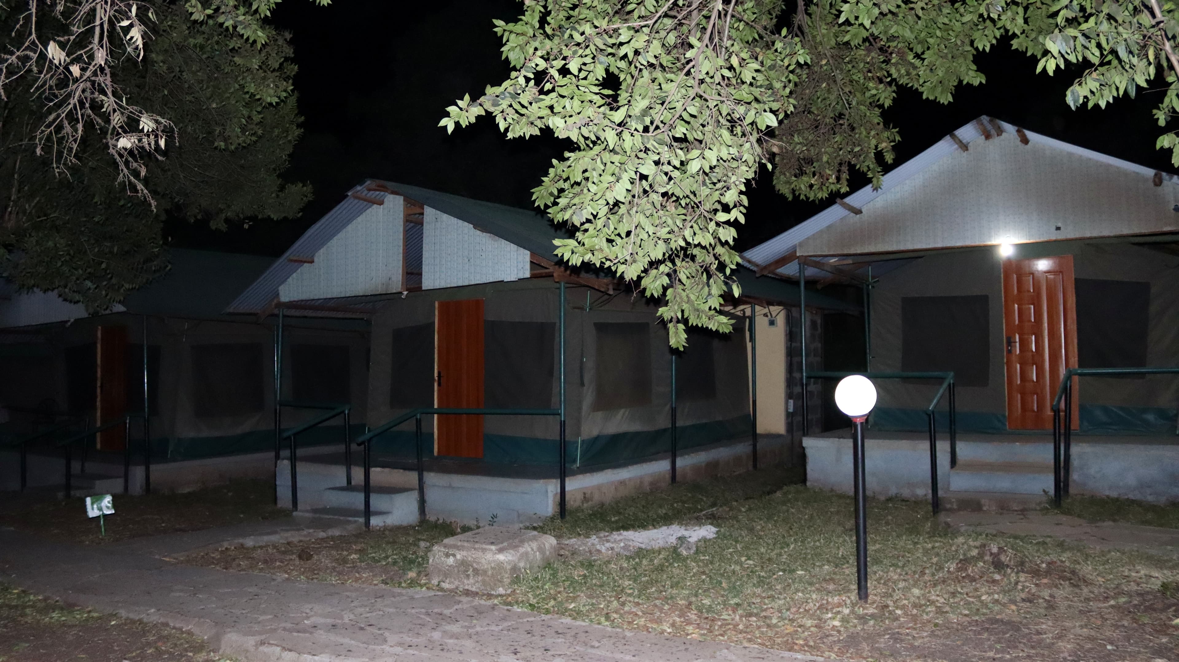 Guest tents lit by porch lights and a garden lamp after dark at Miti Mingi Eco Camp