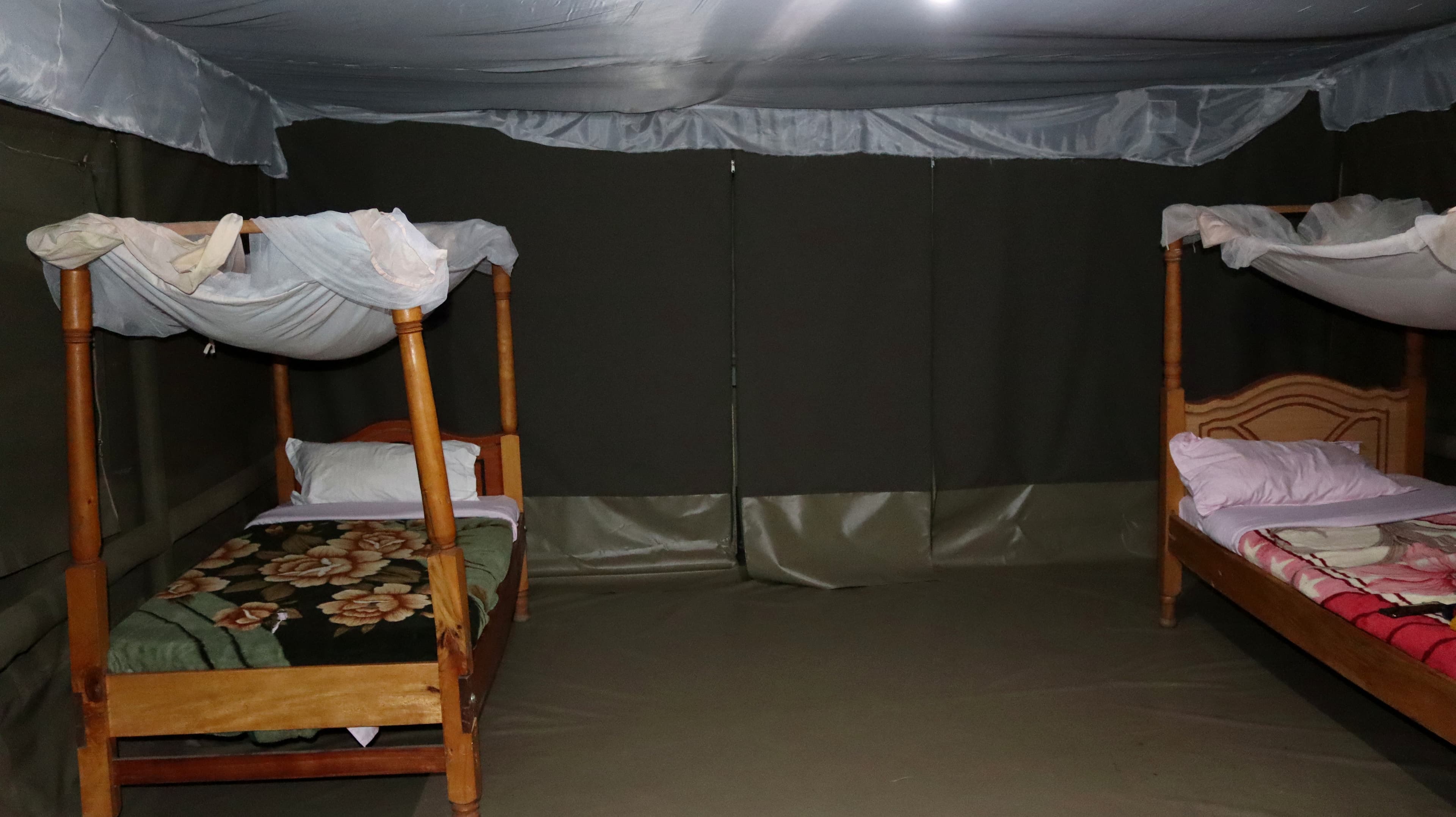 Two beds with canopy mosquito nets on opposite sides of a guest tent at Miti Mingi Eco Camp