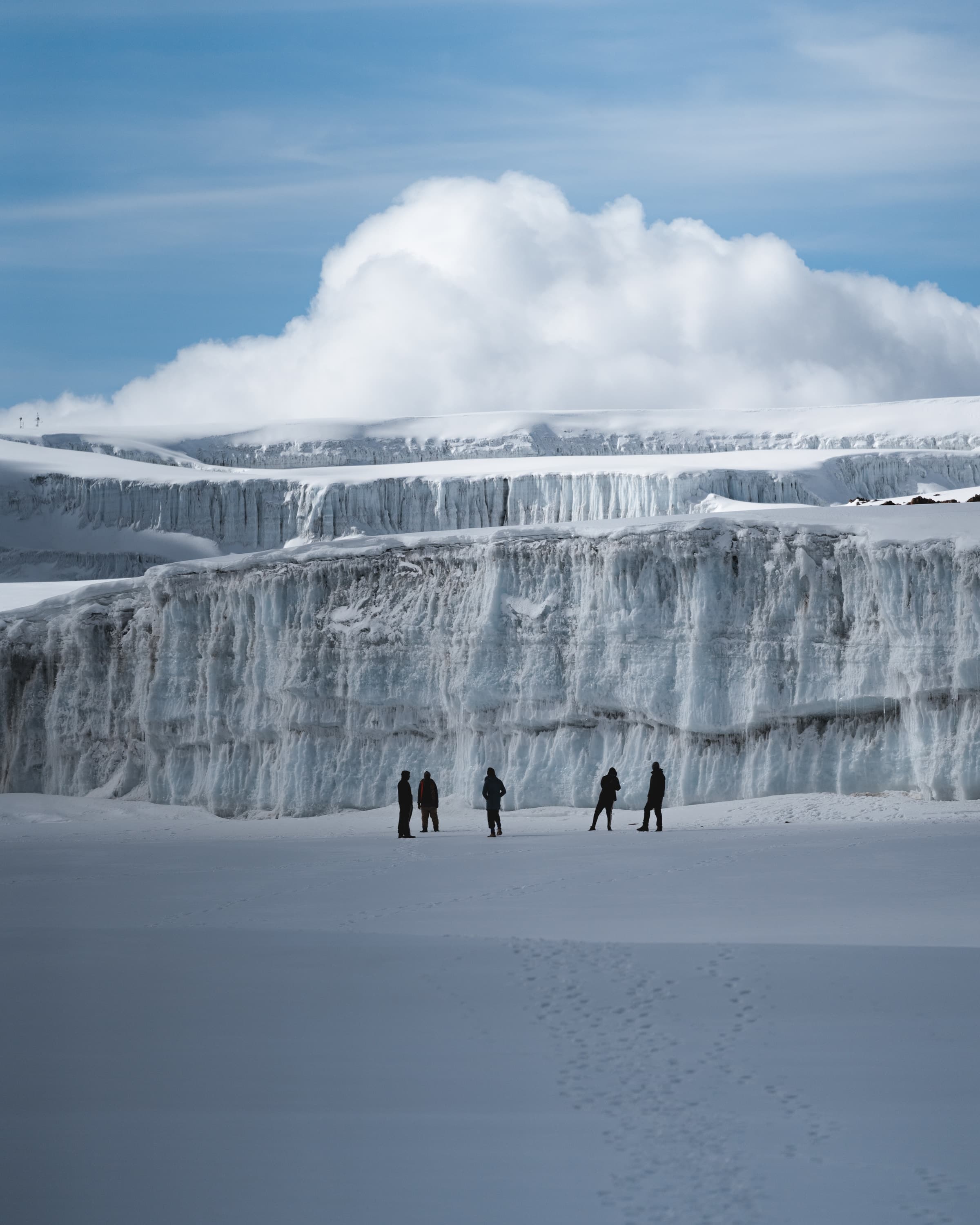 Climbers walking beneath the ice walls of the Northern Icefield on Mount Kilimanjaro